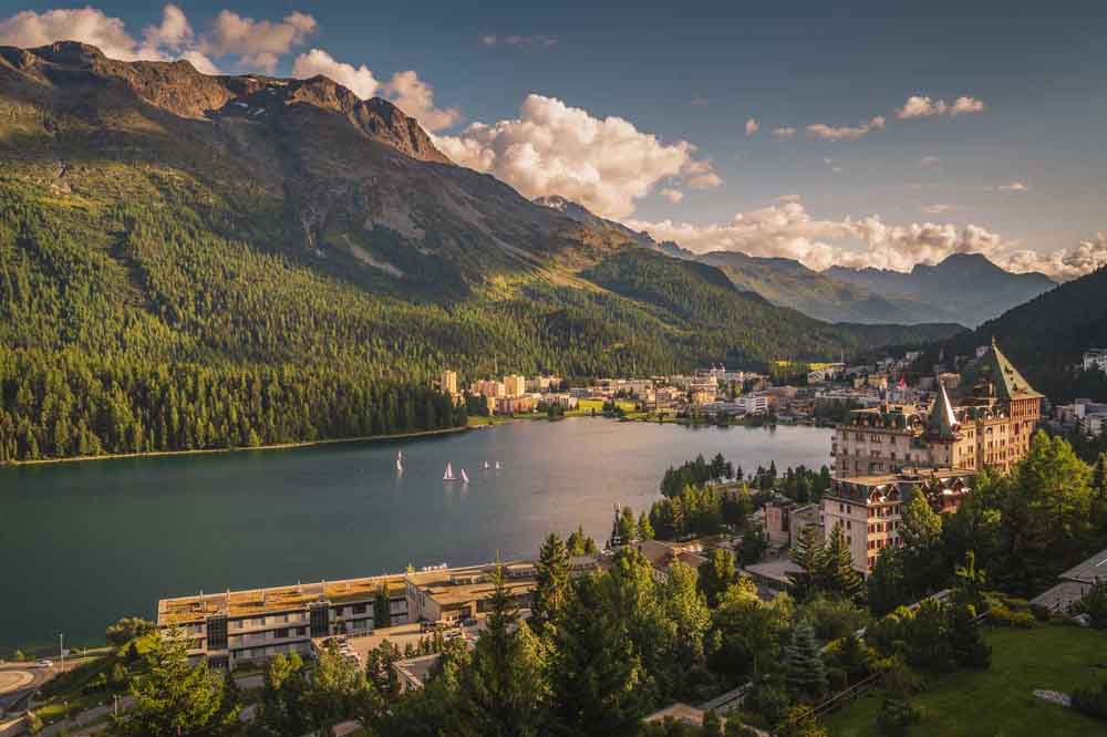 Scenic view of St. Moritz, Switzerland, featuring a serene lake, luxury resorts, alpine forests, and majestic mountain peaks — a top destination for nature lovers and luxury travelers on Switzerland tour packages.