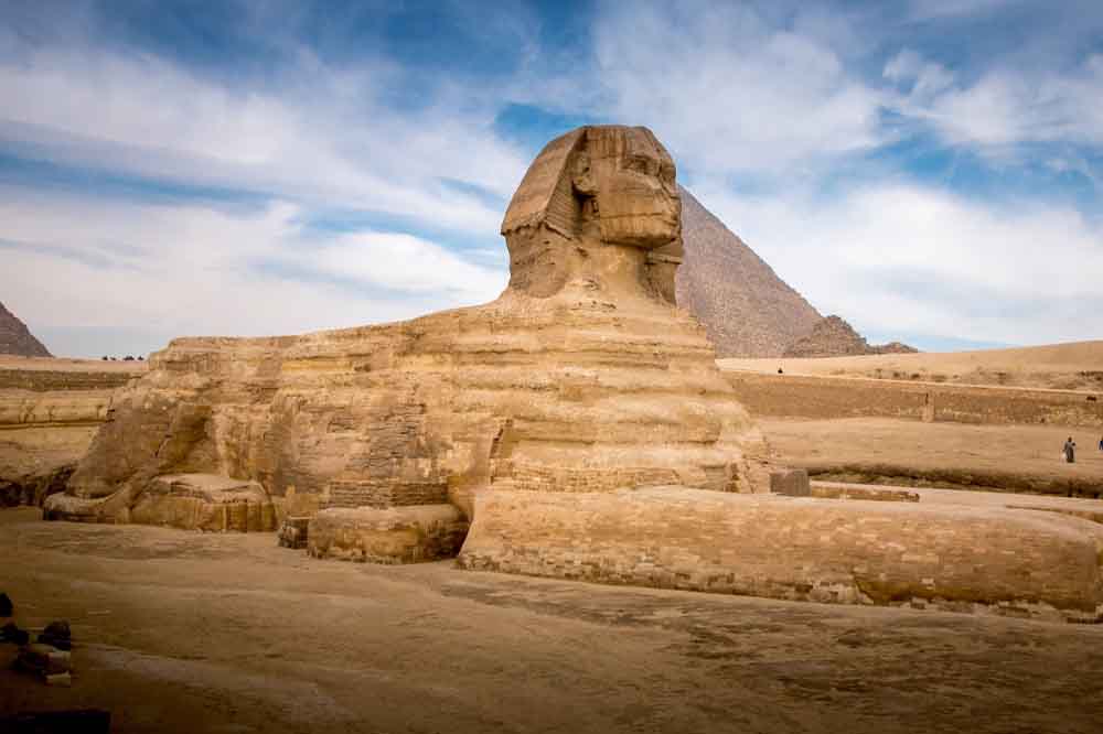 The Great Sphinx of Giza under a blue sky with scattered clouds. The Sphinx, a massive limestone statue, features a human face on a lion's body.
