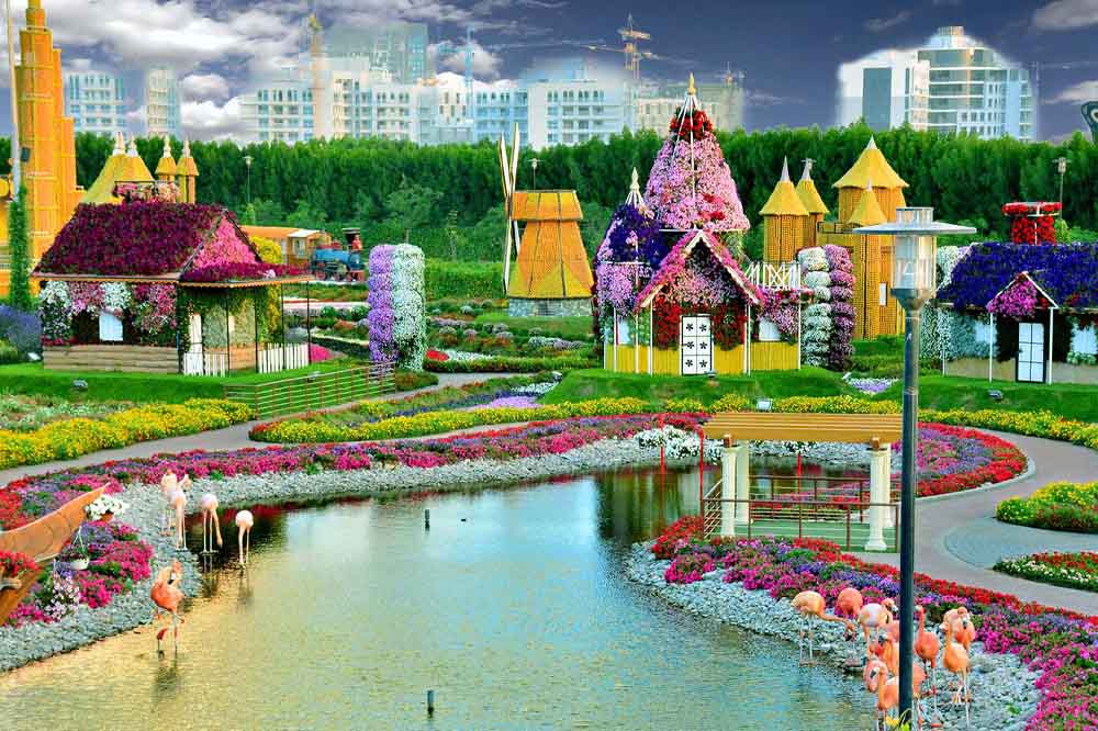 A vibrant garden scene featuring whimsical, floral-covered houses with various colorful blooms. A pond reflects the structures, while flamingos gather at the edge.