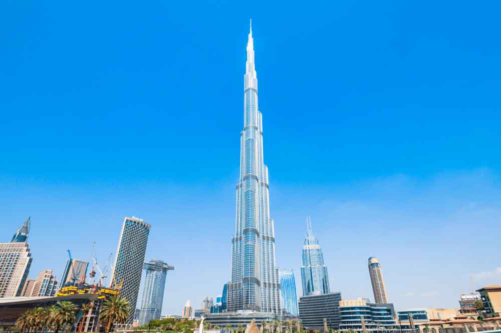 Tall skyscraper set against a clear blue sky in an urban cityscape, surrounded by modern buildings and palm trees, conveying a sense of grandeur.